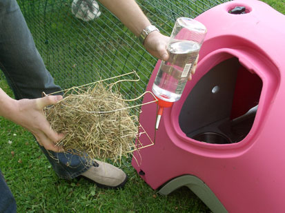 Image of the hay rack and water bottle being placed in the Eglu