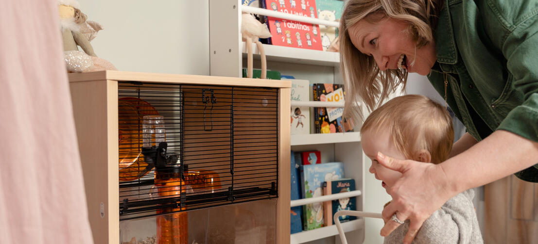 Eine Mutter und ihr Kind schauen begeistert einem Hamster im Qute-Käfig zu.