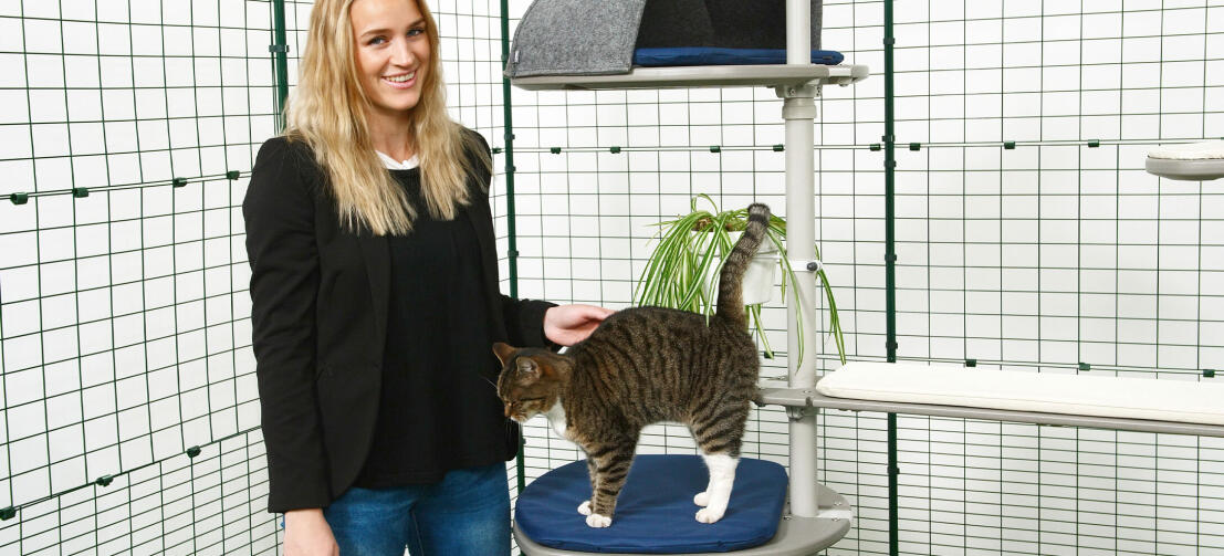 Eine Frau streichelt ihre Katze, die auf dem Freestyle Kletterbaum - Outdoor - spielt