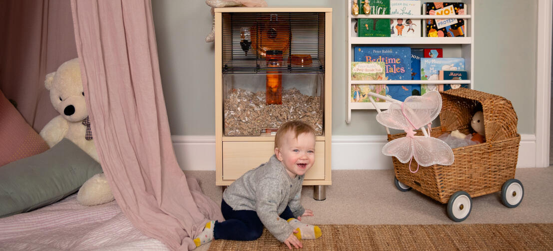 Ein Kleinkind im Spielzimmer vor einem Qute Hamsterkäfig.