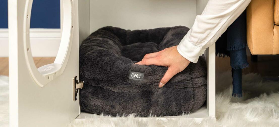 Person, die ein schwarzes Maya donut-katzenbett in ein Maya indoor-katzenhaus stellt