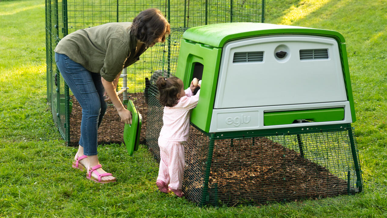 Eine mutter mit ihrer tochter, die in einen modernen hühnerstall greift, um eier zu sammeln