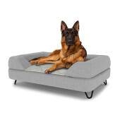 Hund sitzt auf einem großen Topology hundebett mit grauer nackenrolle und schwarzen metall-haarnadelfüßen