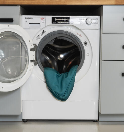 Waschmaschine mit offener tür und kissenbezug in schattiertem fichtenholzdruck innen.