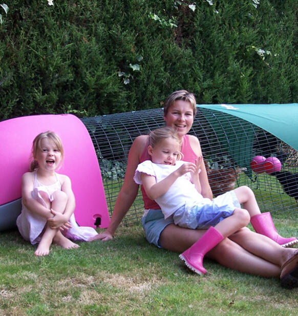 Eine familie sitzt neben einem rosa Eglu hühnerstall