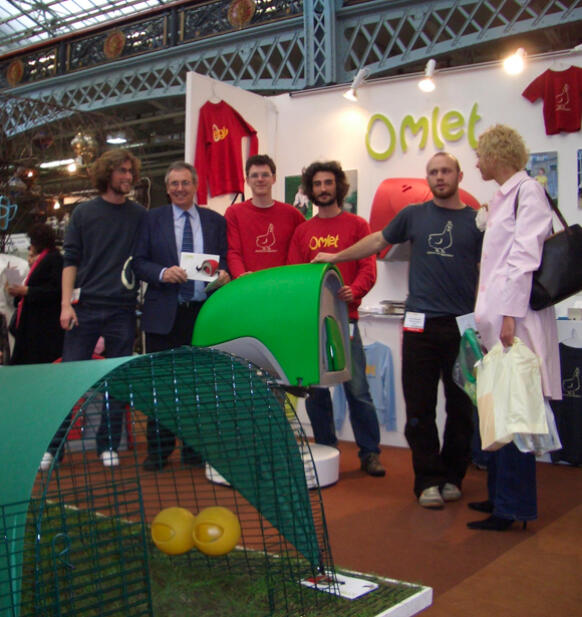 Eine gruppe von menschen, die an einem stand mit dem Eglu Cube hühnerstall posieren