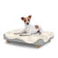 Hund sitzt auf einem kleinen Topology hundebett mit schafsfellauflage und runden holzfüßen