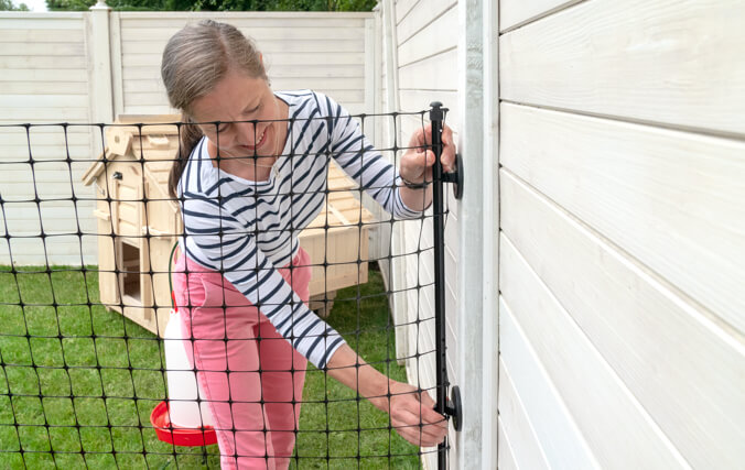 Eine Frau befestigt den Omlet Hühnerzaun an eine Holzmauer im Garten