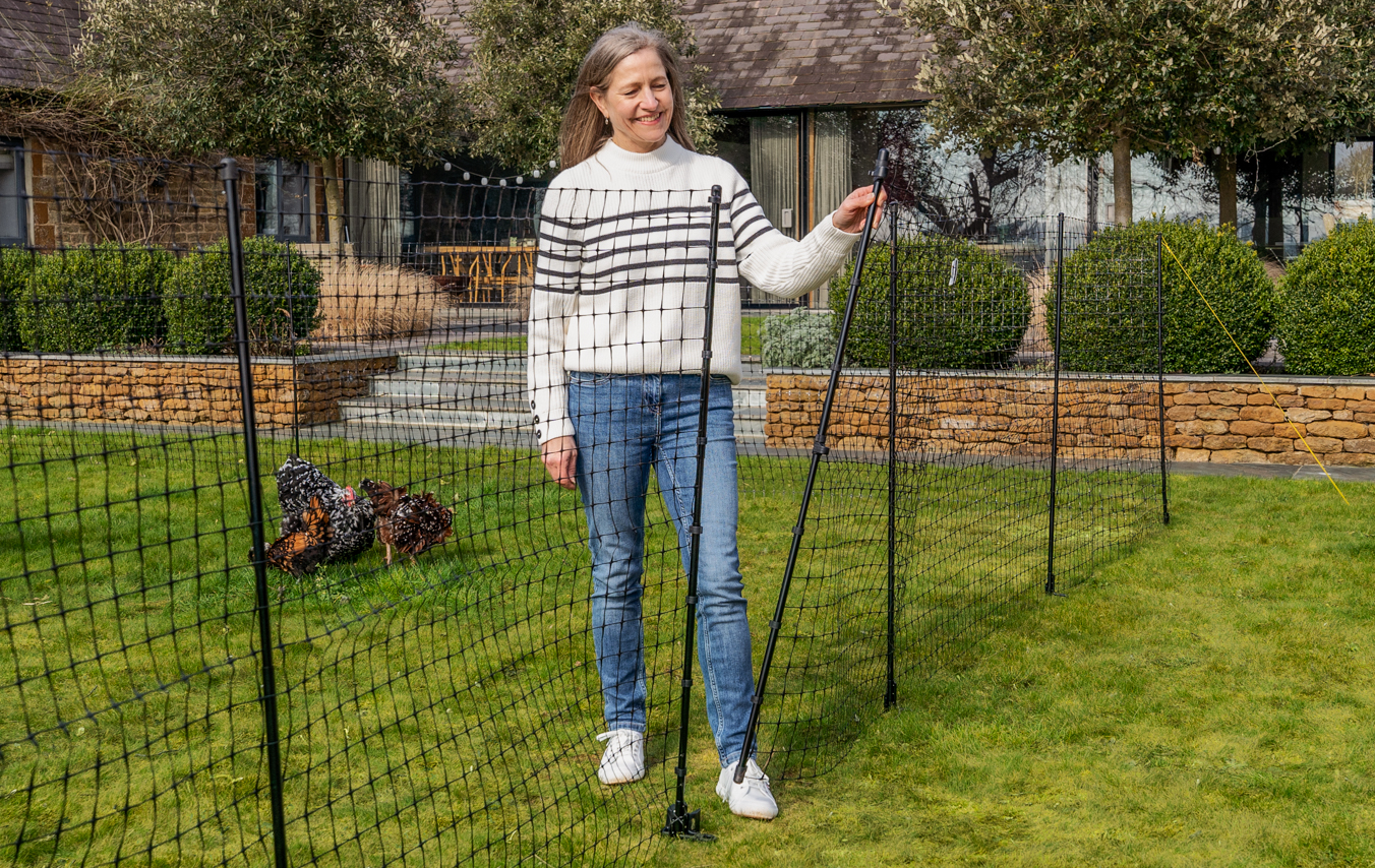 Der Hühnerzaun im Garten mit einer Frau, die das eingebaute Tor schließt