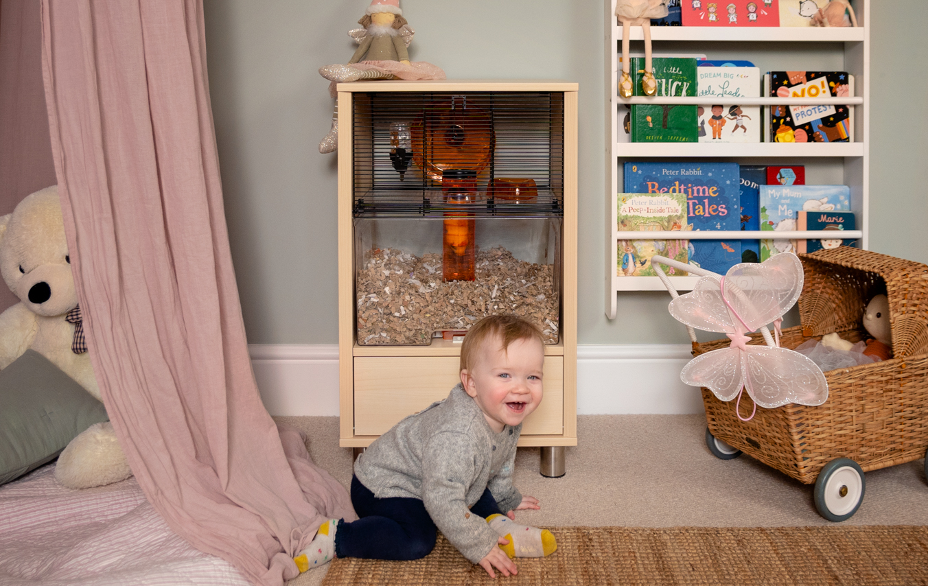 Ein Kleinkind beim Spielen im Kinderzimmer mit dem Qute Hamsterkäfig im Hintergrund
