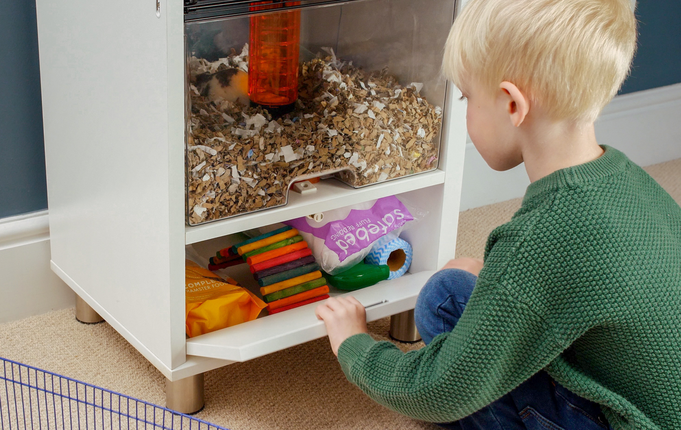 Ein Kind legt die Hamstereinstreu in den Stauraum des Qute Hamsterkäfigs