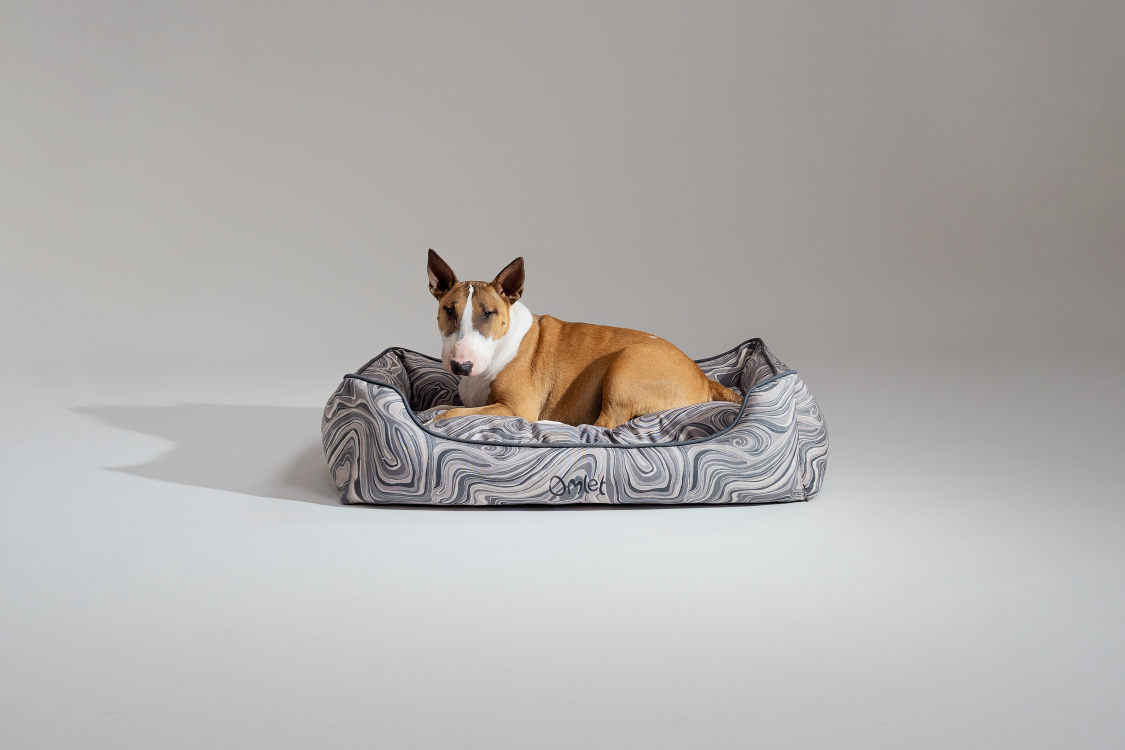 Ein English bull terrier relaxing on their Omlet Nest Dog Bed in Contour Grey